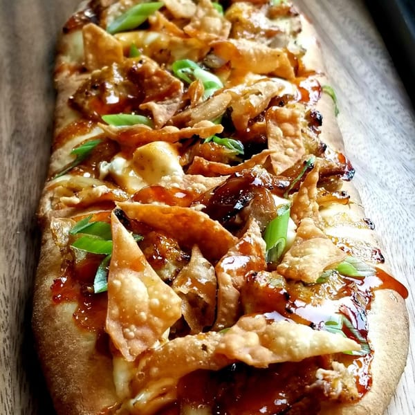 Close-up of a flatbread pizza topped with crispy wontons, sweet chili sauce, and green onions.