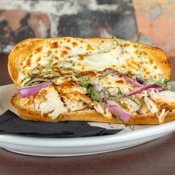 Chicken sub sandwich with melted cheese, red onions, and greens on a white plate.