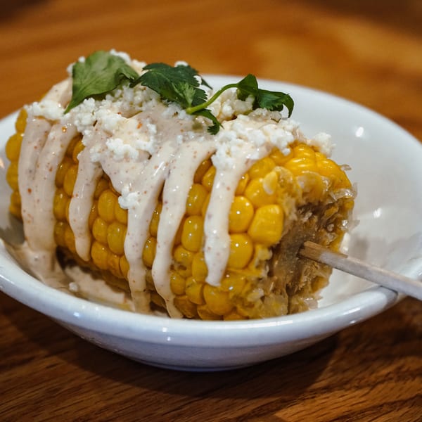 Elote, Mexican street corn, on a white dish with crema, cotija cheese, and cilantro.