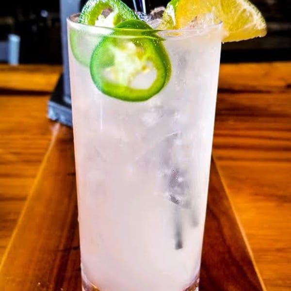 A refreshing cocktail with jalapeño slices and a lime wedge on a wooden bar top.