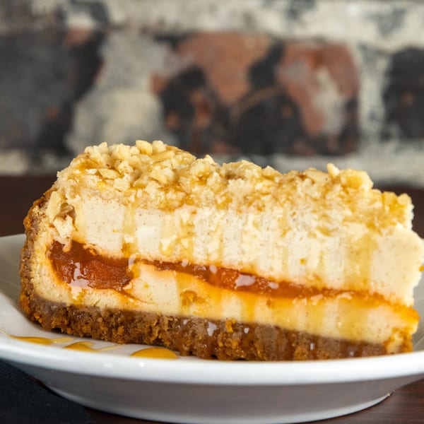 A slice of cheesecake with a graham cracker crust, caramel filling, and crumb topping.