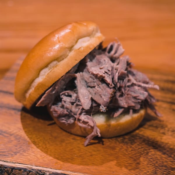 A delicious pulled beef sandwich on a wooden board, with the top bun slightly askew.
