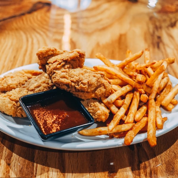 Crispy fried chicken tenders with a side of golden french fries and dipping sauce on a wooden table.