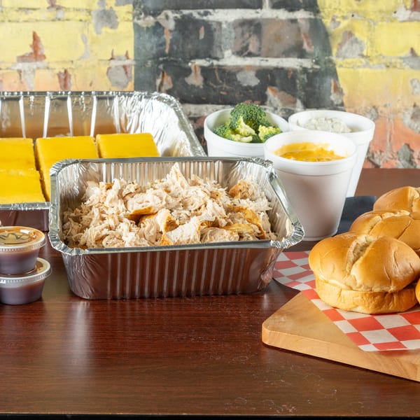 Catering spread with pulled chicken, cornbread, broccoli, mac and cheese, rolls, and sauces.