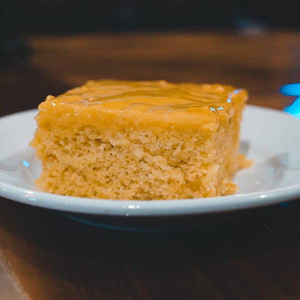 A square slice of golden cake with a shiny, thick glaze on a white plate.