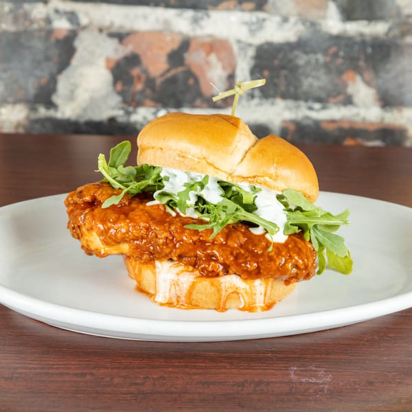 Spicy fried chicken sandwich with arugula and white sauce on a white plate.