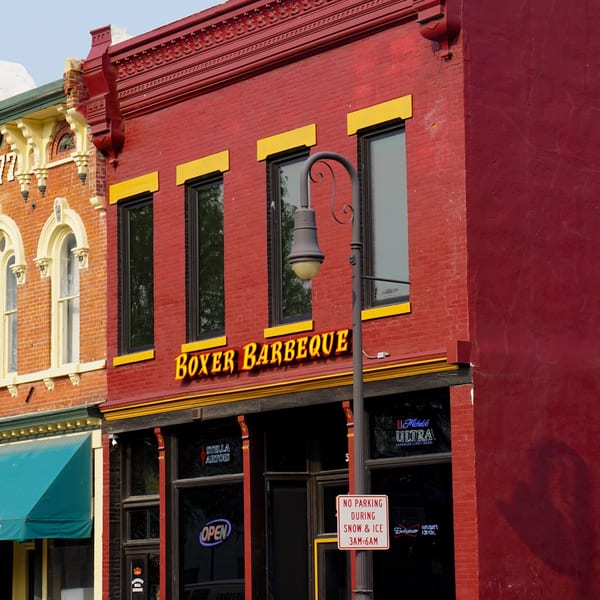 The red brick facade of Boxer Barbeque restaurant with yellow trim and large windows.