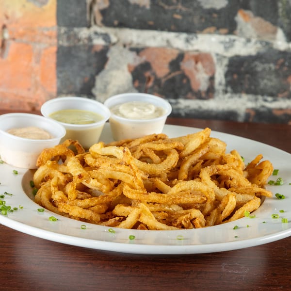 A white plate piled high with crispy golden onion rings, garnished with chives and three dipping sauces.