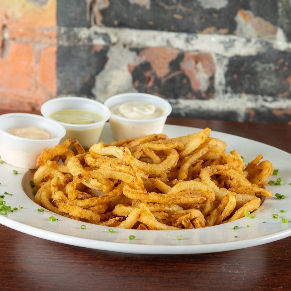 A white plate piled high with crispy golden onion rings, garnished with chives and three dipping sauces.