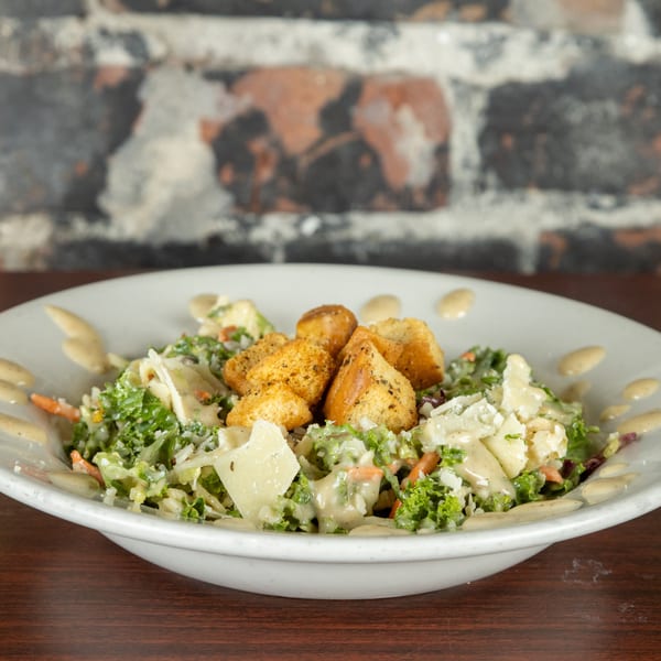 A Caesar salad with croutons, shaved parmesan, and dressing in a white bowl on a wooden table.