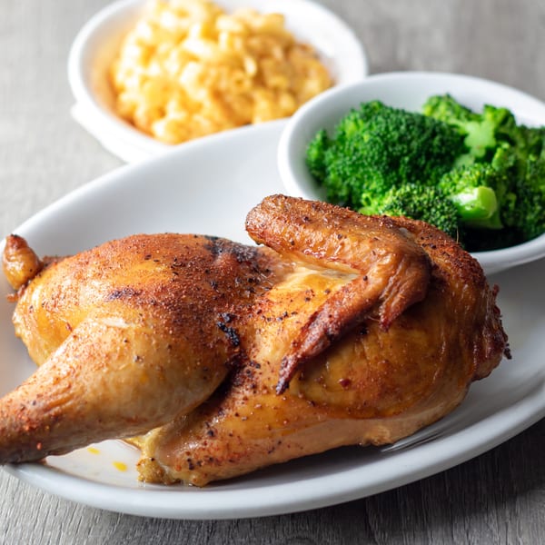 A roasted chicken half with crispy skin, served with sides of bright green broccoli and macaroni and cheese.