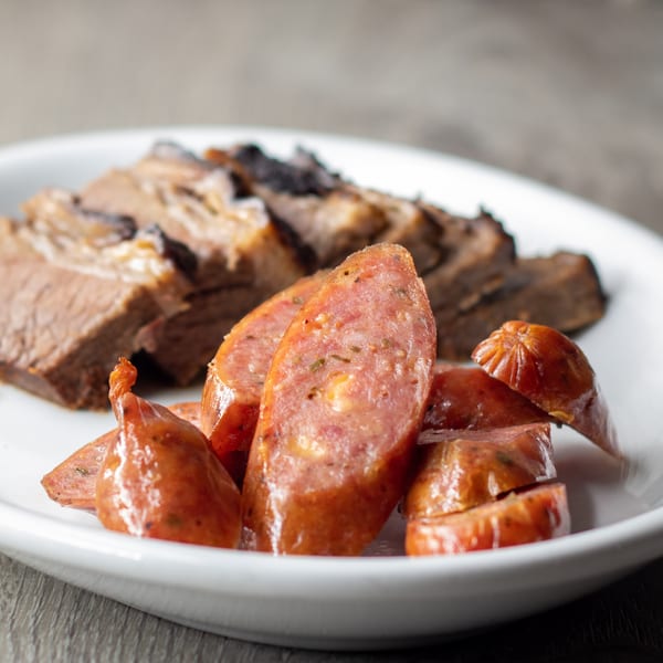 Sliced smoked sausage and brisket on a white plate, ready to be served.