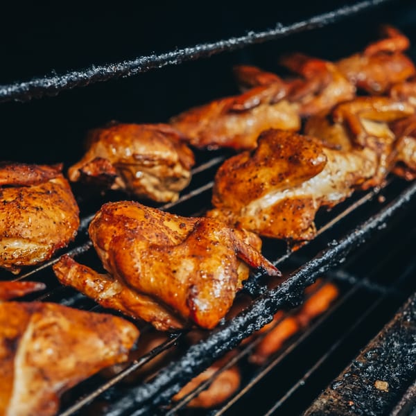 Golden brown chicken pieces, seasoned and grilling on a dark, smoky barbecue rack.