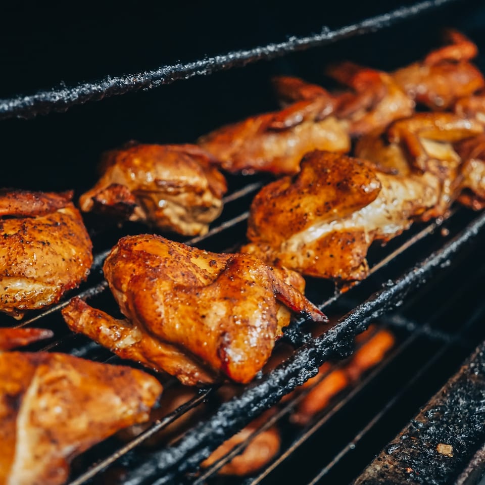 Golden brown chicken pieces, seasoned and grilling on a dark, smoky barbecue rack.