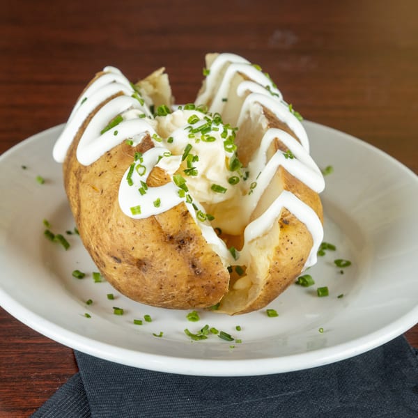 Baked potato topped with sour cream, butter, and chives on a white plate.